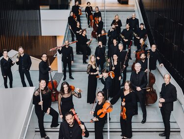 Orchestra in black attire with instruments on staircase