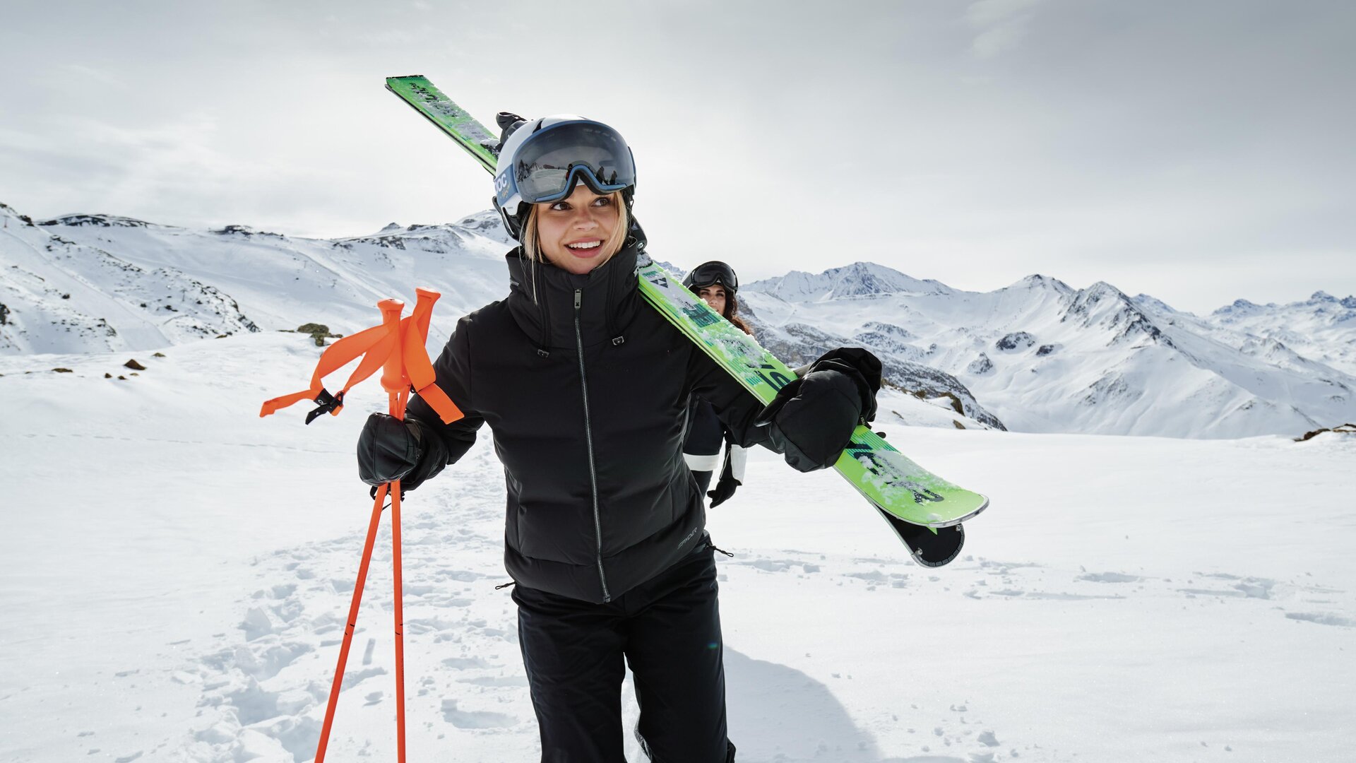 Ein Skifahrer fährt mit Schwung die Piste hinunter. Im Hintergrund sind schneebedeckte Berge und ein klarer Himmel zu sehen.