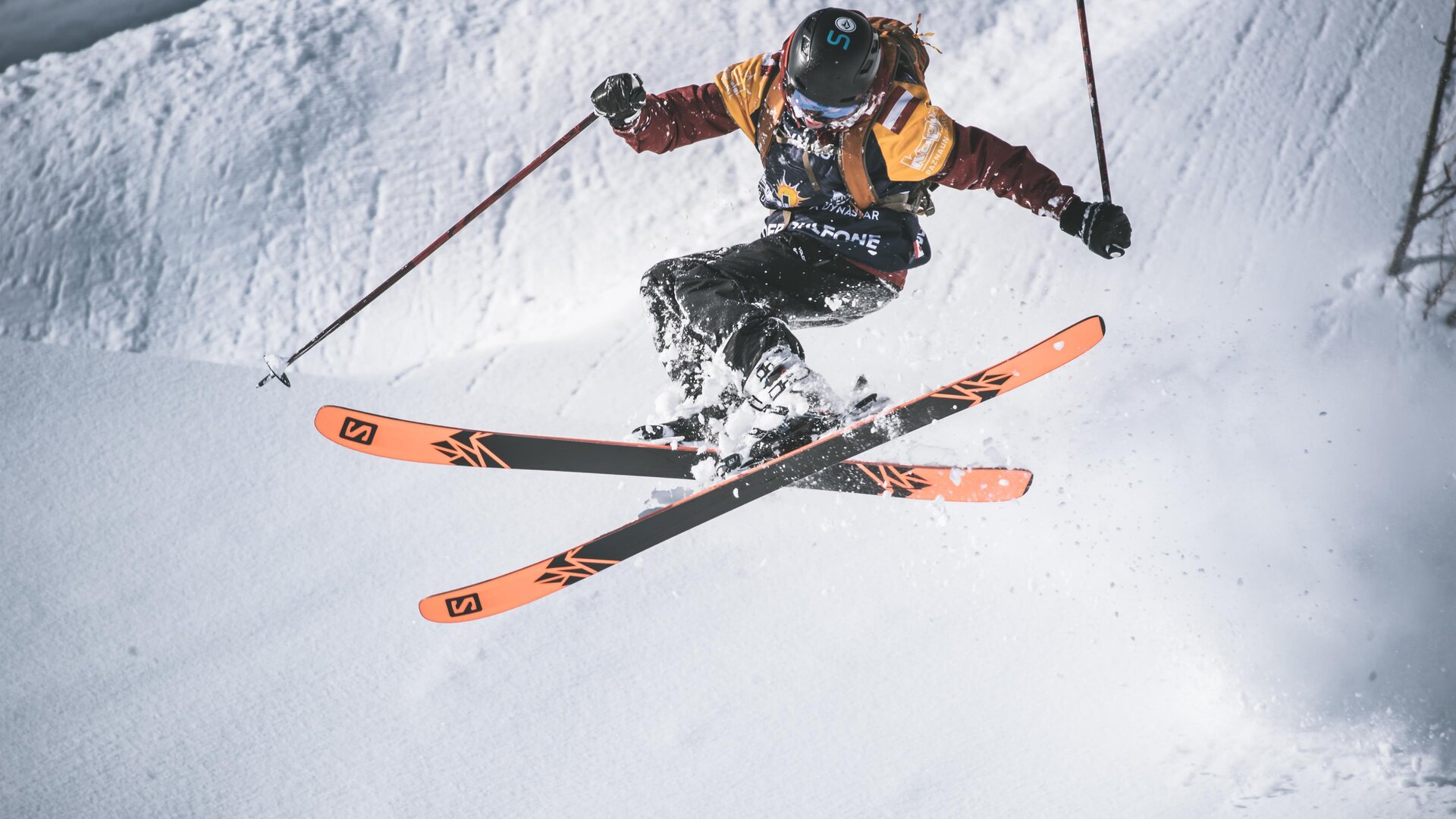 A skier jumps over a snow-covered slope. He is wearing colorful ski gear and showcasing impressive technique.