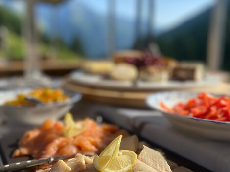 Eine ansprechend angerichtete Auswahl an Fischplatten, garniert mit Zitrone. Im Hintergrund sind weitere Speisen und eine schöne Landschaft zu sehen.