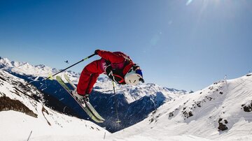 A skier jumps over a snow hill in the mountains. The sky is clear and the sun is shining brightly.