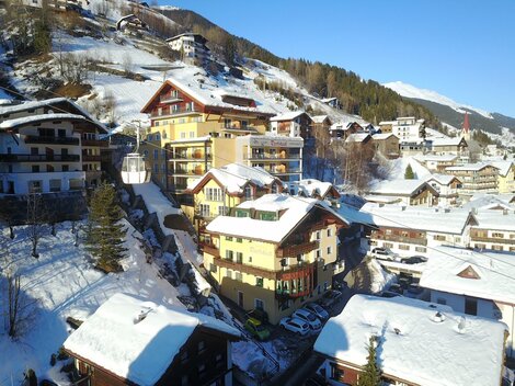 Eine malerische Winterlandschaft mit schneebedeckten Dächern und traditionellen Holzgebäuden. Die Berge im Hintergrund vervollständigen das idyllische Bild.