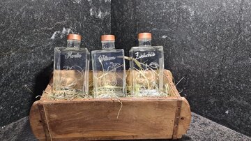 Three glass bottles in a wooden container, surrounded by hay. The bottles are sealed with corks and labeled.