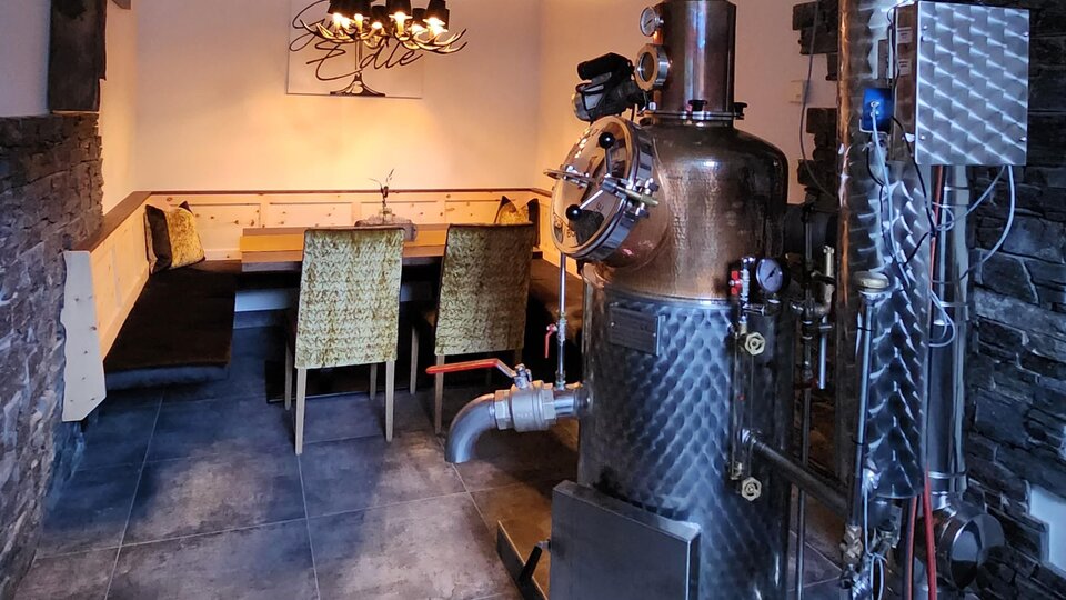 A cozy room with a large distillation device. In the background, several chairs are arranged around a table.