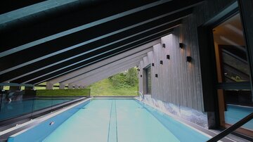 A modern indoor pool in an architecturally appealing space. The large window offers a view of the green surroundings.