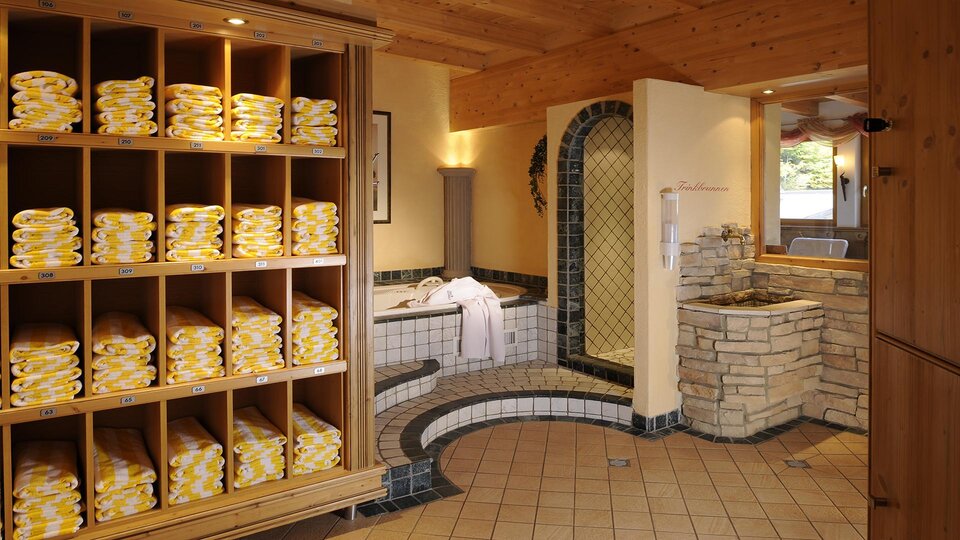 A relaxing wellness area with neatly stacked towels on shelves. In the background, a whirlpool and an inviting sauna can be seen.