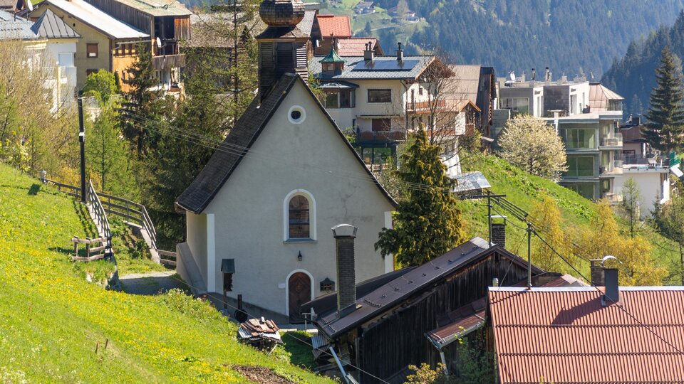 Ein malerisches Dorf in den Bergen mit einer kleinen Kirche. Die Umgebung ist grün und von beeindruckenden Hügeln umgeben. | © Bernhard Gruber – Photography