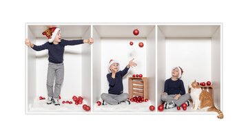A cheerful child in a white room, playing with red balls. A cat sits nearby and watches. | © Simone Drexel Photography