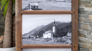 A wooden frame with three black-and-white photographs of landscapes and a church. In the background, there are mountains and a calm lake. | © Simone Drexel Photography