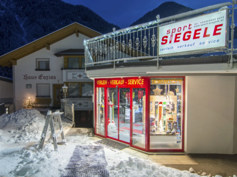 Ein Sportgeschäft mit großen Fenstern, das in einer verschneiten Umgebung bei Dämmerung steht. Das Gebäude hat eine gemütliche Atmosphäre und liegt in den Bergen.