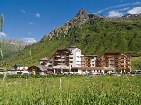 A beautiful hotel in the mountains with green meadows and a blue sky. The surrounding landscape is picturesque and inviting.
