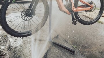 A high-quality mountain bike is being washed. In the background, a building with a balcony can be seen.