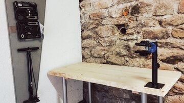A simple workplace with a wooden table and a sturdy stand. Various tools are hanging on the wall in a storage.