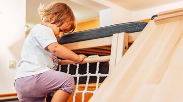 A small child is climbing on a play structure with a net. They are wearing a T-shirt and pants and are focused on climbing.