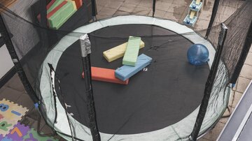 A trampoline on a balcony, surrounded by safety nets. Colorful foam mats and a ball lie on the mat.
